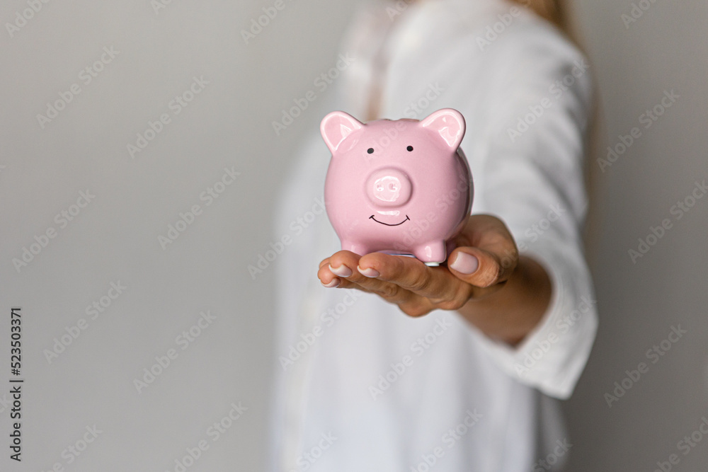 female hands puts a coin in a pink piggy bank. The concept of saving money or savings, investment female hands puts a coin in a pink piggy bank. The concept of saving money or savings, investment