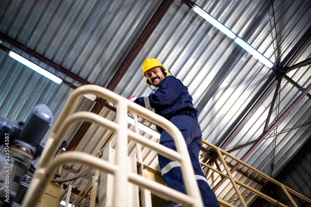 Portrait of factory worker climbing on metal platform in production plant.