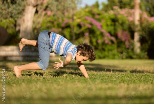Mischievous preschooler boy somersaults on sand grass in the park.