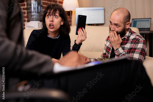 Angry wife accusing husband of cheating and marriage betrayal, having proof of adultery at therapy session. Couple in divorce crisis attending meeting with therapist, couseling advice. photo