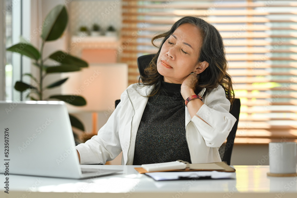 Middle aged businesswoman rubbing neck, suffering from neck pain during workplace at home Middle aged businesswoman rubbing neck, suffering from neck pain during workplace at home
