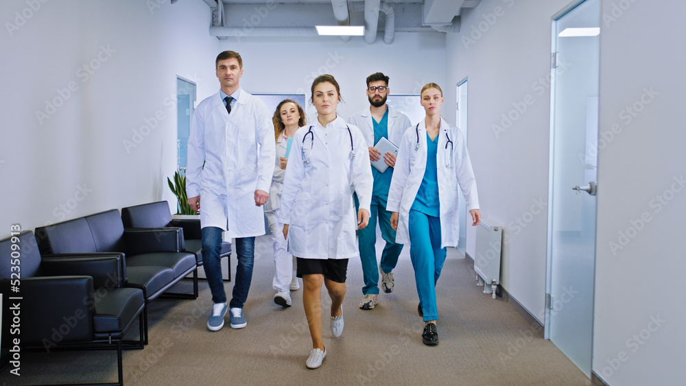 Young and mature team of doctors and nurses walking in front of the camera in the hospital corridor looking straight to the camera concept of medicine and health care Young and mature team of doctors and nurses walking in front of the camera in the hospital corridor looking straight to the camera concept of medicine and health care