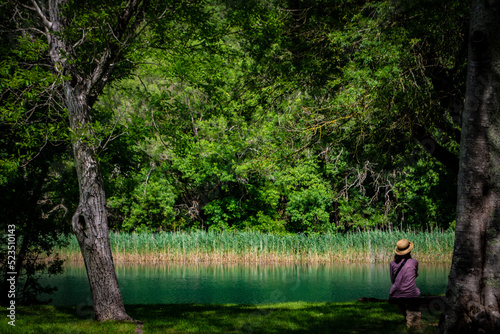 romantic girl sitting on the bank of the river, by the trees, Krka, Kistanje, Croatia, green and turquoise, lake © sarns
