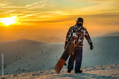 Snowboarder walking with snowboard during sunset in the mountains