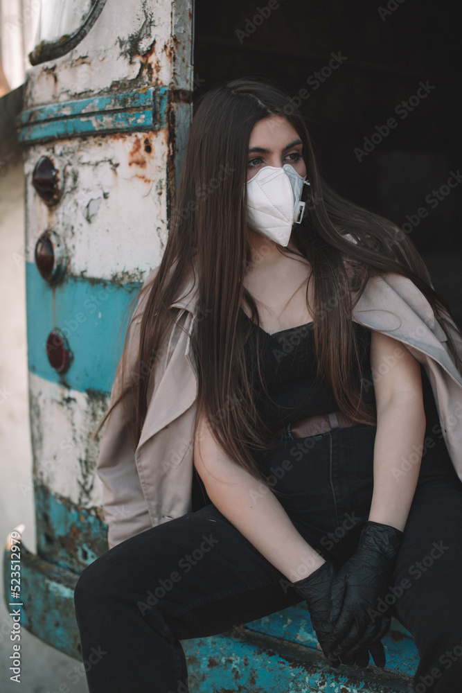 Naklejka premium A beautiful girl with long hair in a respirator protecting against a virus in a broken bus in a post-apocalyptic world. 