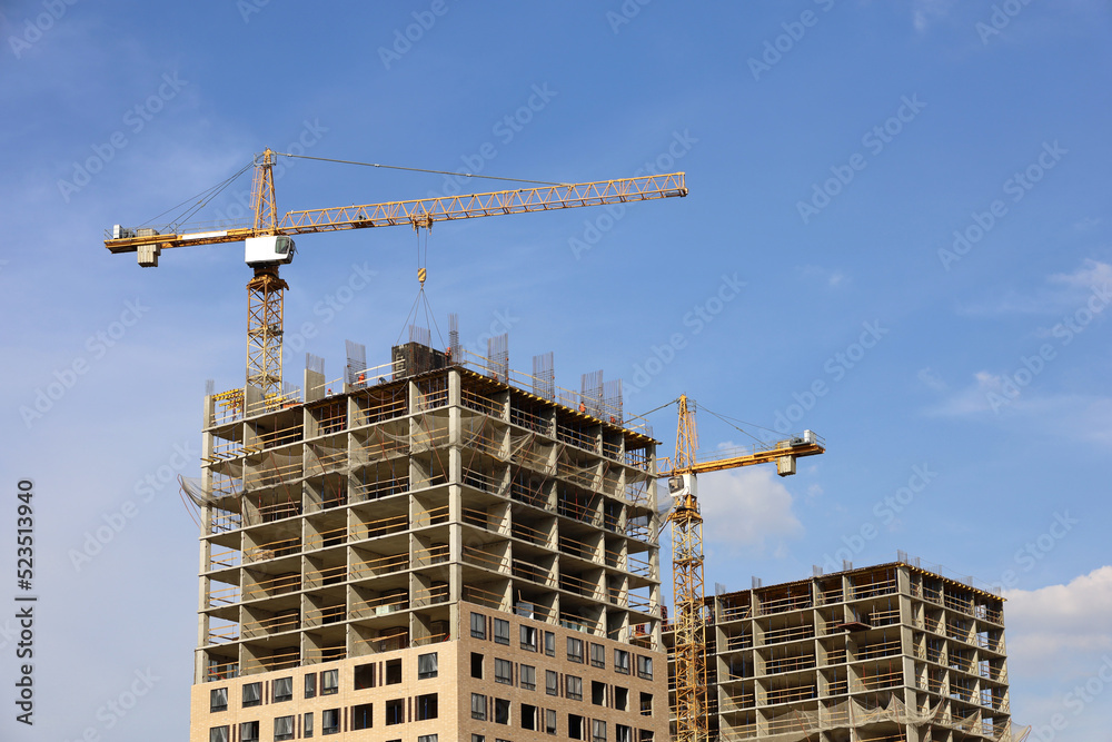 Tower cranes and unfinished buildings on background of blue sky with white clouds. Housing construction, apartment blocks in city Tower cranes and unfinished buildings on background of blue sky with white clouds. Housing construction, apartment blocks in city
