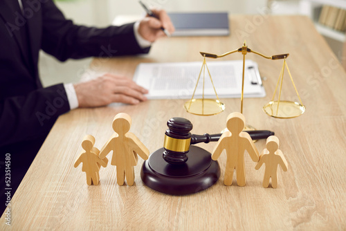 Figures of family are separated by judge's gavel, which symbolizes divorce case and custody of child. Close up of wooden figurines of people on background of judges and scales of justice. photo