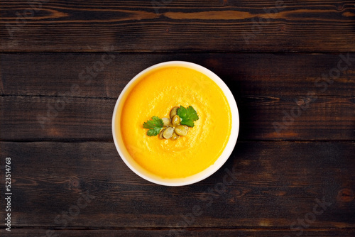 Pumpkin soup in a bowl, sprinkled with pumpkin seeds on dark wooden background, top view.