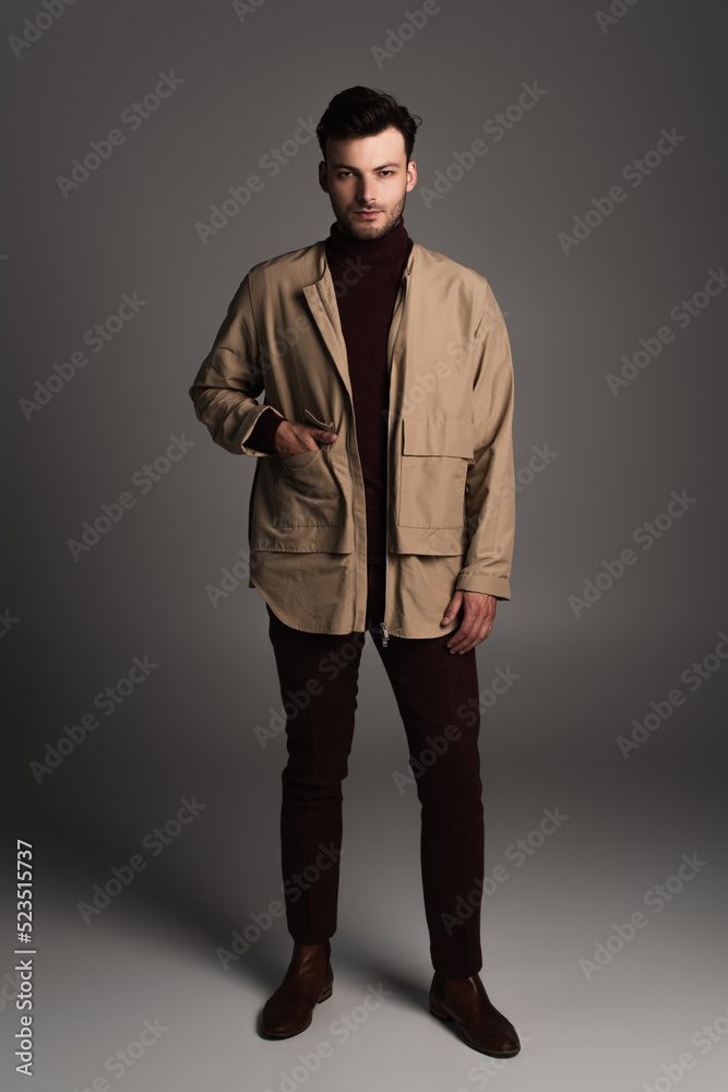 Young brunette man in autumn jacket standing on grey background.