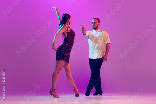 Beautiful coupleof dancers in adorable attires dancing ballroom dance isolated on purple background. Concept of art, beauty, music, style.