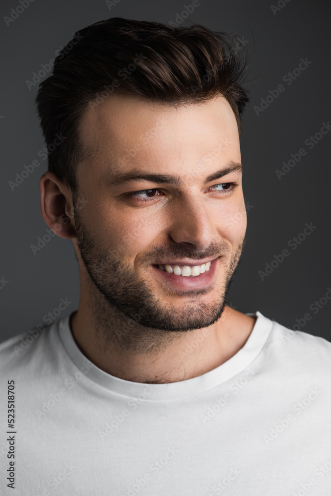 Portrait of bearded and smiling man in white t-shirt looking away isolated on grey. Portrait of bearded and smiling man in white t-shirt looking away isolated on grey.