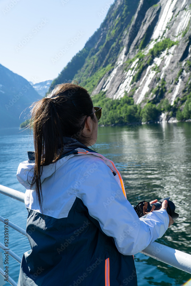 Unrecognizable young woman traveling by ferry with her camera visiting the famous Geirangerfjord and its waterfalls.
