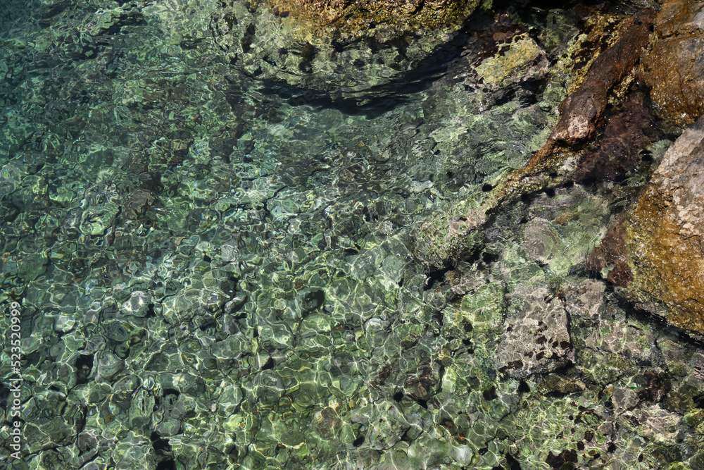 Shallow water with rocky sea bottom as background, top view