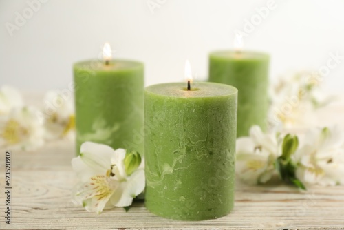 Burning candles and beautiful flowers on white wooden table