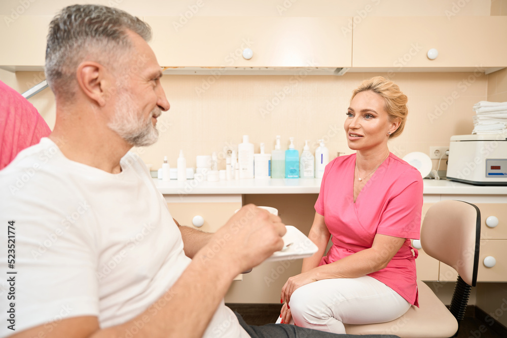 Fototapeta premium Beautician consulting patient drinking coffee in office