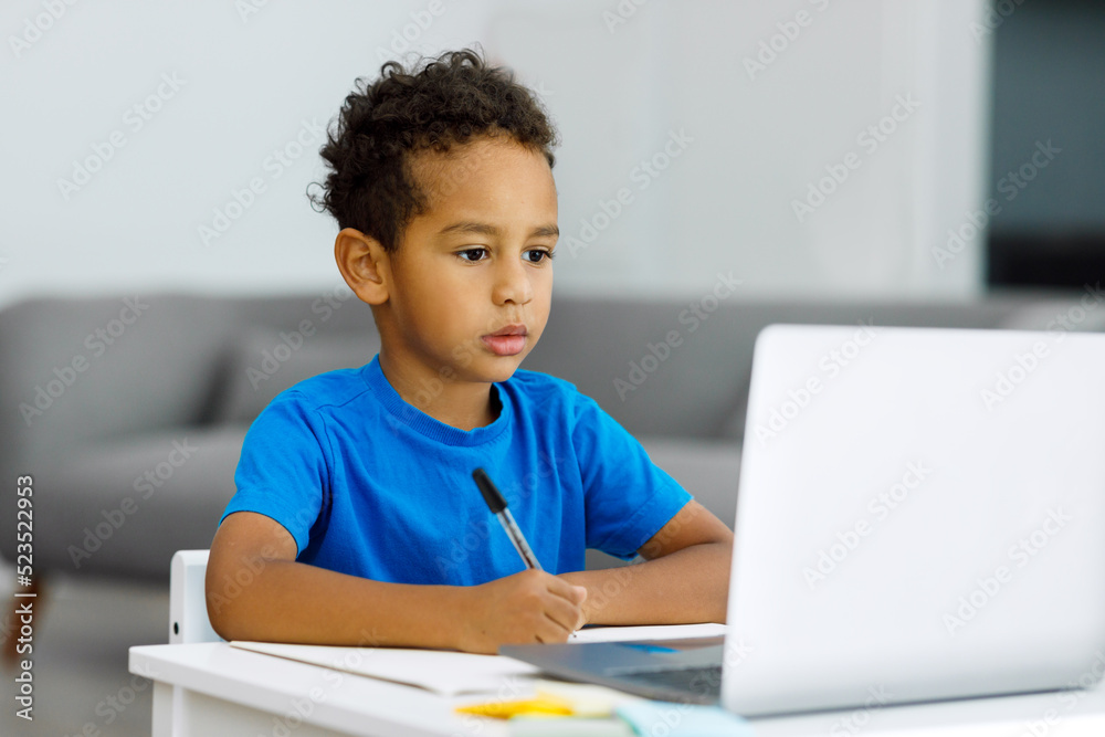 African American boy doing homework on a laptop computer while sitting at a table indoors. African American boy doing homework on a laptop computer while sitting at a table indoors.