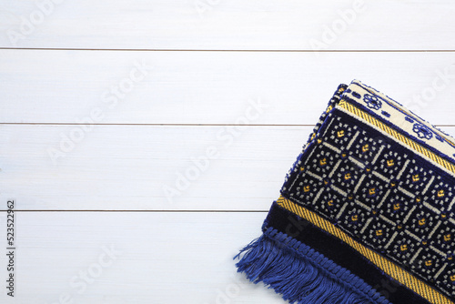 Muslim prayer rug on white wooden table, top view. Space for text