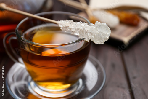 Stick with sugar crystals and cup of tea on wooden table, closeup