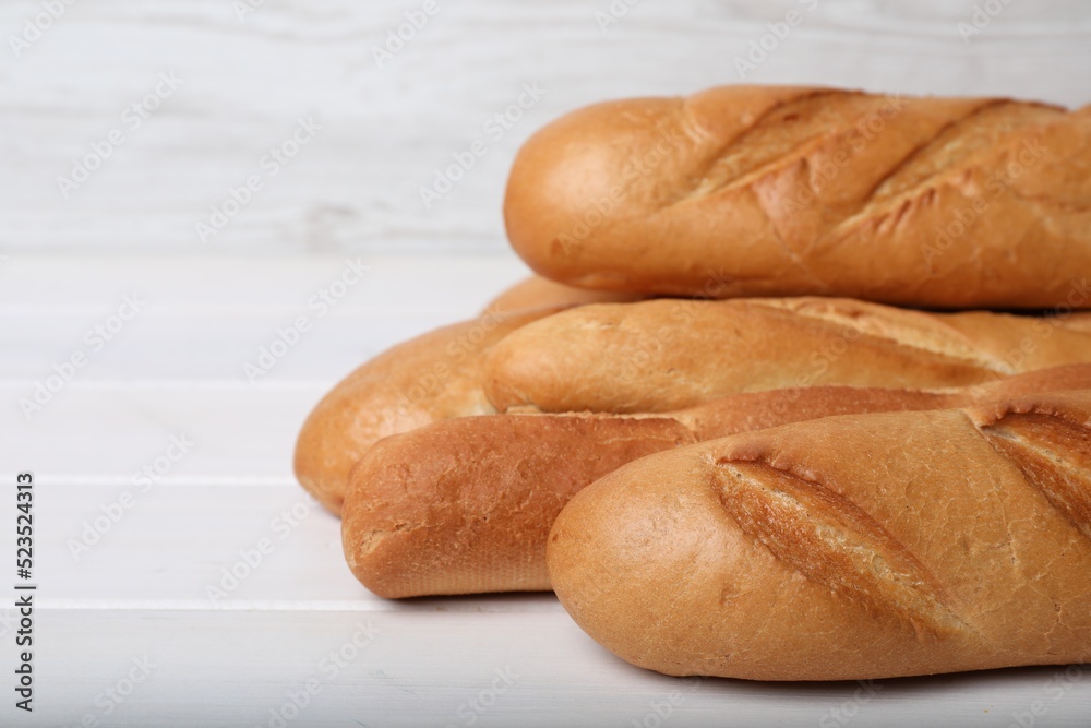 Tasty baguettes on white wooden table, closeup. Space for text