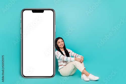 Photo of charming adorable brunette hair girl sit next to big phone promotion placard isolated on teal color background