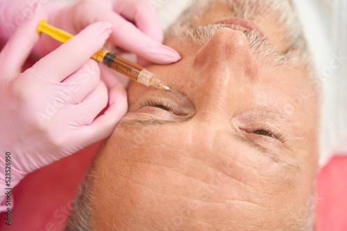 Beautician hands making beauty injection to man under eye