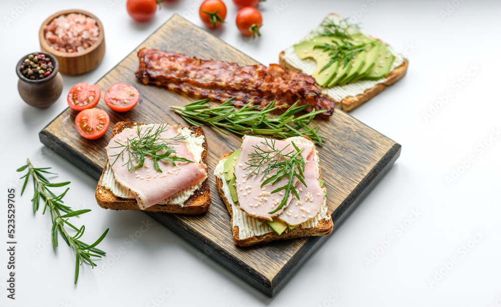 Fresh, delicious ham, butter, avocado and sesame seeds sandwiches on a wooden cutting board Fresh, delicious ham, butter, avocado and sesame seeds sandwiches on a wooden cutting board