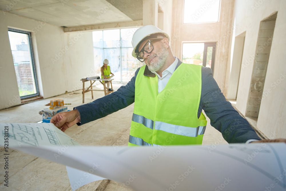 Male foreman holds expanded drawing and speaks on mobile phone Male foreman holds expanded drawing and speaks on mobile phone