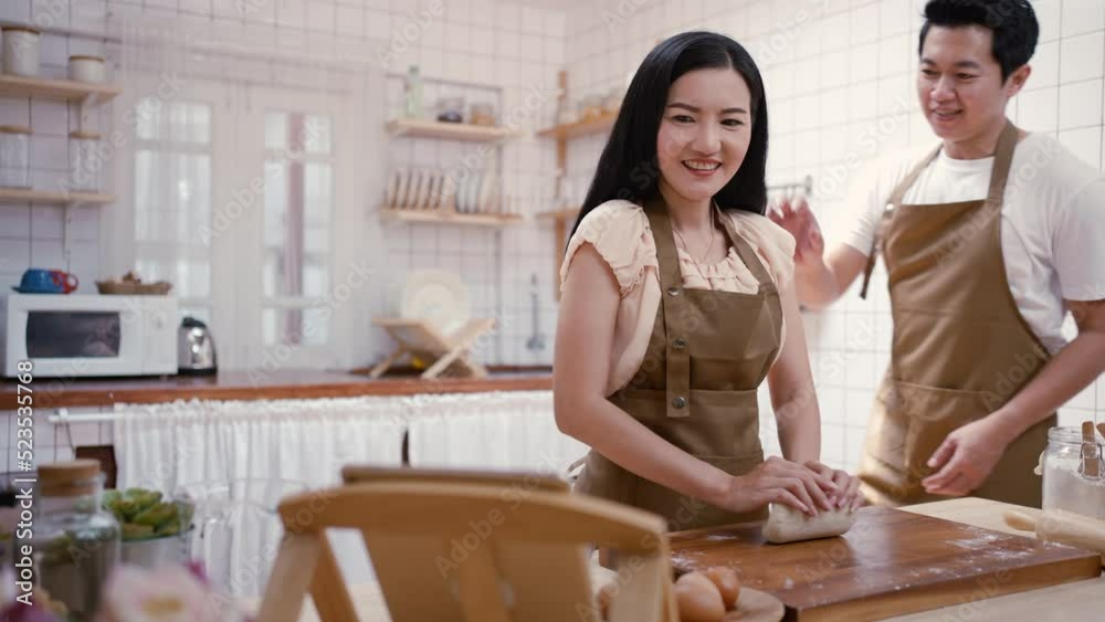 Asian new marriage couple stay home, spend time together in kitchen. Attractive young man and woman looking to how to make dessert on tablet knead yeast dough with hands for baking bakery in house Asian new marriage couple stay home, spend time together in kitchen. Attractive young man and woman looking to how to make dessert on tablet knead yeast dough with hands for baking bakery in house