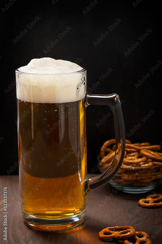 Organic craft cold wheat beer alcohol beverage served in drinking glass with dense foam or froth and crunchy salted snack crackers on dark brown wooden table at bar or restaurant for refreshment Organic craft cold wheat beer alcohol beverage served in drinking glass with dense foam or froth and crunchy salted snack crackers on dark brown wooden table at bar or restaurant for refreshment