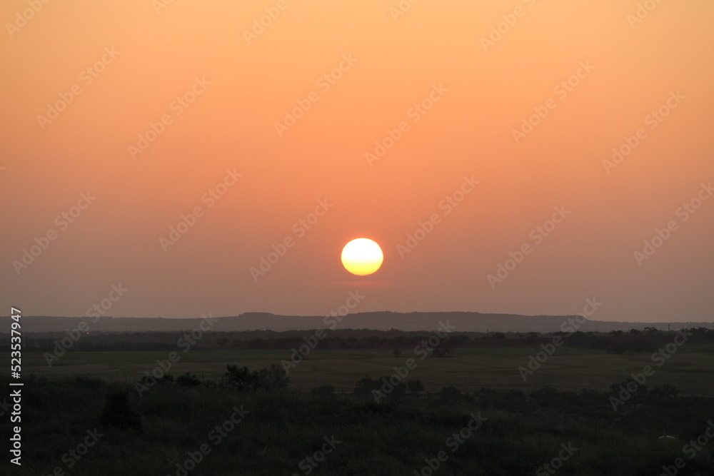 Sunrise creating red skyline over valleys and mountains of West Texas, with flare stacks in distance