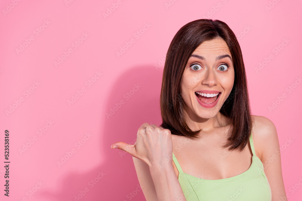 Photo of shiny excited young lady wear green dress pointing thumb back empty space isolated pink color background Photo of shiny excited young lady wear green dress pointing thumb back empty space isolated pink color background