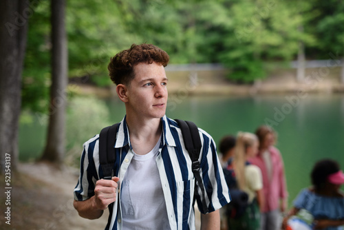 Portrait of young man with friends at background on a hiking or camping trip in the mountains in summer.