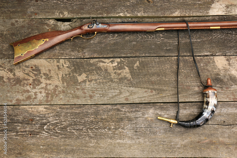 Traditional kentucky rifle and a gunpowder horn on an old, damaged
