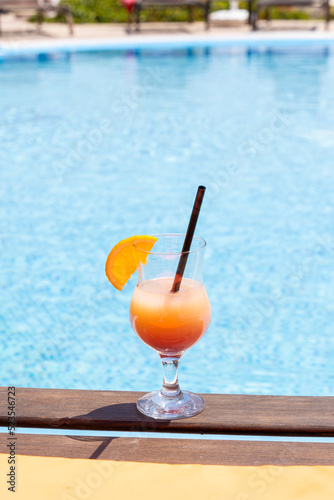 Fresh glass of a cocktail with an orange slice on the border of a swimming pool. Holiday and vacation concept.