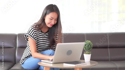 Close-up of a young woman sitting on a couch while she works on her laptop at the adjacent coffee table.  Title space photo