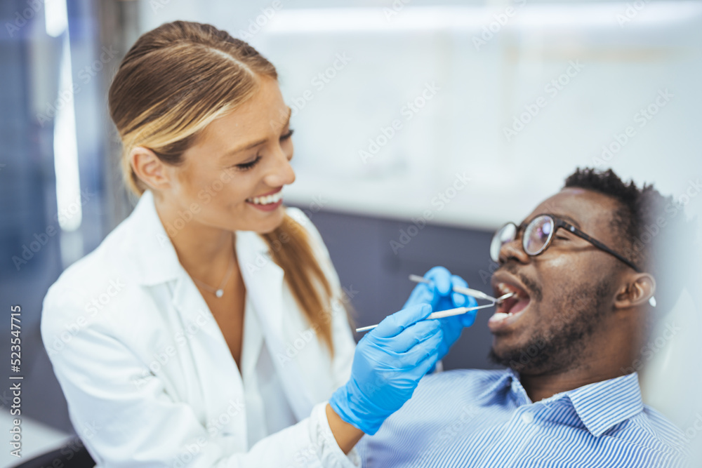 Close up portrait of smiling black man and dentist doctor hands holding tools. African American young man having a visit at the dentist's. He is sitting on chair at dentist office in dental clinic. Close up portrait of smiling black man and dentist doctor hands holding tools. African American young man having a visit at the dentist's. He is sitting on chair at dentist office in dental clinic.