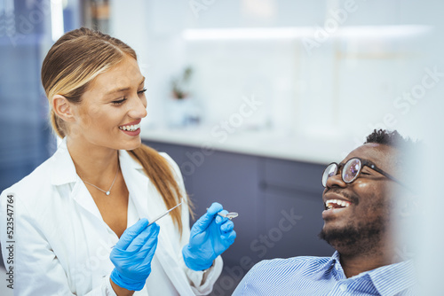 Smiling african guy in dentist chair looking with trust at his doctor, close up. Young African American Man Getting Teeth Treatment With Professional Stomatologist At Modern Clinic