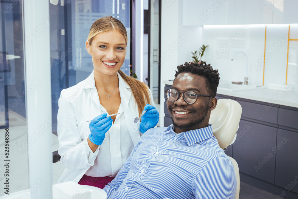 My dentist is the best! Portrait of a female dentist and young man in a dentist office. Happy dentist and patient in dentist's office. African guy in dentist chair smiling at camera, close up.. My dentist is the best! Portrait of a female dentist and young man in a dentist office. Happy dentist and patient in dentist's office. African guy in dentist chair smiling at camera, close up..
