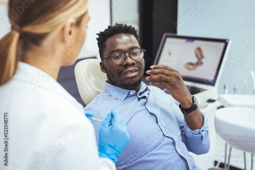Young good looking man having dental treatment at dentist s office. African guy in dentist chair looking with trust at his doctor  close up. Man having teeth examined at dentists.