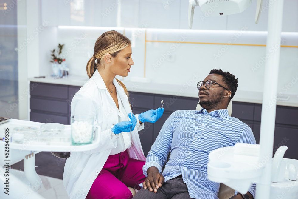 Obraz premium Young man patient having dental treatment at dentist's office. Female dentist working on patient's teeth. Man having teeth examined at dentists. Overview of dental caries prevention