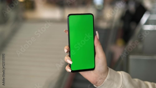 View of a woman on the phone with a green screen for copy space. Chromakey mockup without tracking markers. Close up.Young woman standing in a shopping mall with a smartphone. Busy shopping center photo