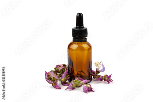 A bottle of essential oil with fresh blooming clary sage twigs on white background.