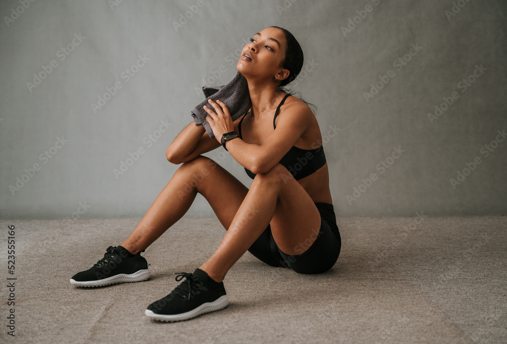 Multi Ethnic female sitting on the floor wiping her neck with her towel after work out Multi Ethnic female sitting on the floor wiping her neck with her towel after work out
