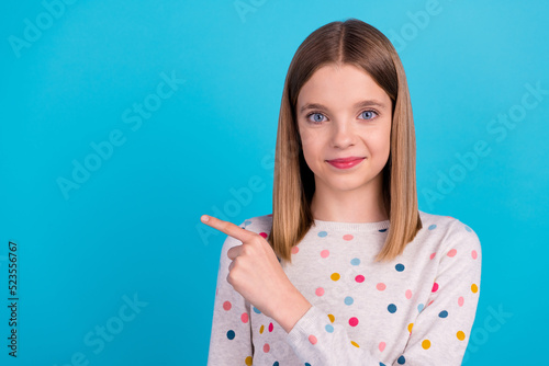 Photo of funky cute small girl wear dotted shirt smiling pointing empty space isolated blue color background
