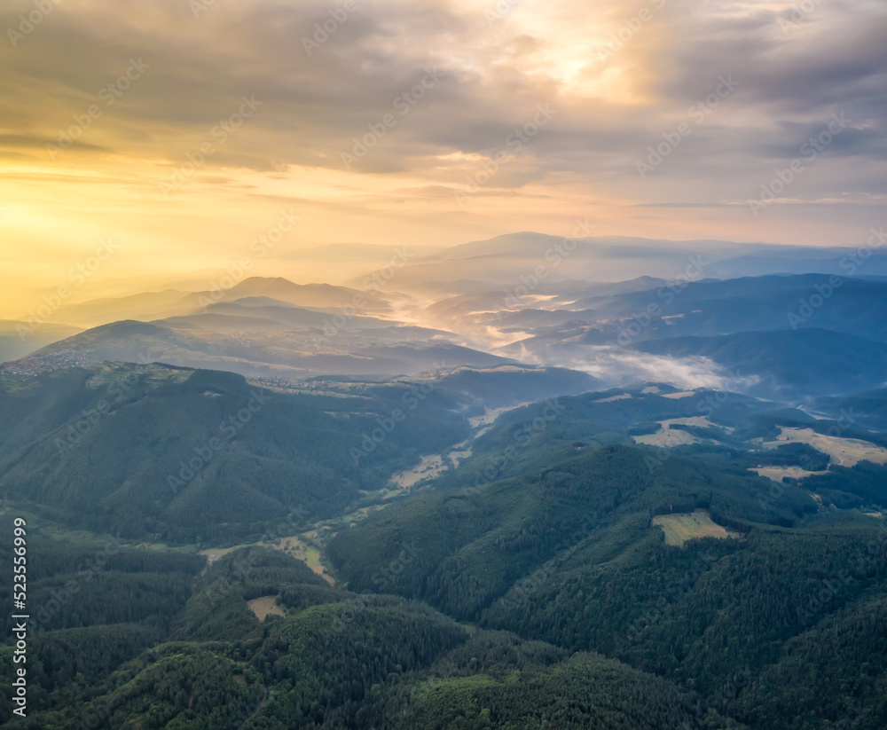 Amazing aerial view of beautiful low clouds creeping on the tree-covered mountain slopes, the Rhodopes in Bulgaria at sunrise.
