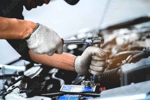 Close-up shot of working in a repair and maintenance service garage. Auto mechanic working on car engine in mechanics repair service garage. A uniformed mechanic is working on a car service. © KANGWANS