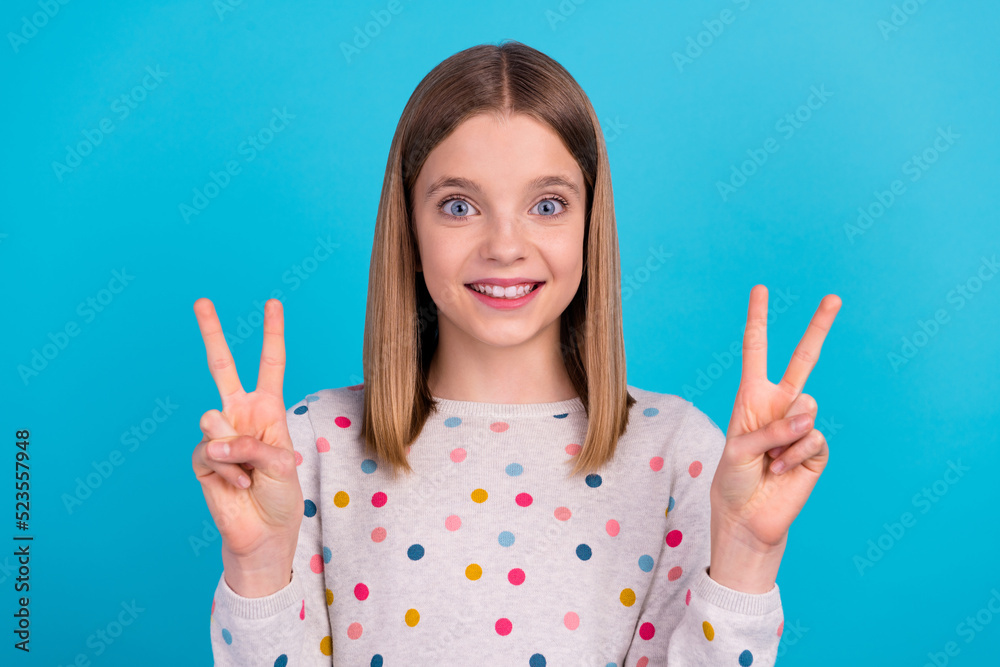 Photo of pretty funky small girl wear dotted shirt smiling showing two v-sings isolated blue color background Photo of pretty funky small girl wear dotted shirt smiling showing two v-sings isolated blue color background