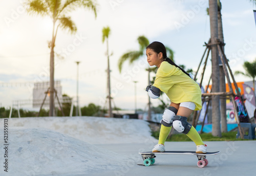 asian child skater or kid girl playing skateboard or riding surf skate up to wave ramp or wave bank to fun bottom turn in skate park by extreme sports to wear elbow pads knee support for body safety