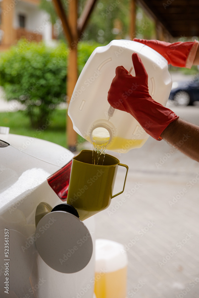 Gasoline collapse. A man pours gasoline from a large canister into a petrol tank of a car. Fuel shortage in the country. A man refuels his car