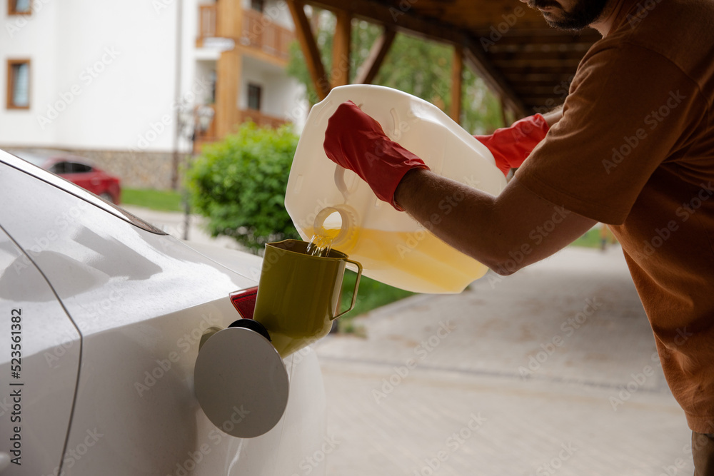 Gasoline collapse. A man pours gasoline from a large canister into a petrol tank of a car. Fuel shortage in the country. A man refuels his car